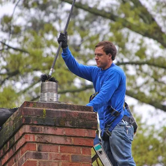 Technician brushing a metal flue from a residential rooftop